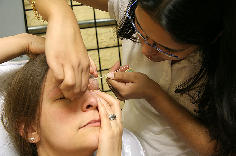 Rinku Shah is "threading" Caroline's eyebrows - the Indian way of plucking eyebrows.