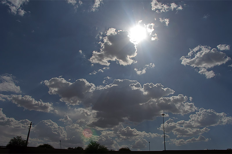 The sun peeking out from behind small clouds over Phoenix, Arizona