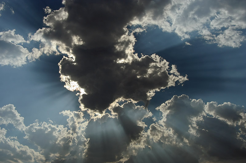 The sun is behind a dark narrow but tall cloud with dramatic sun rays extending out from the edges of the cloud